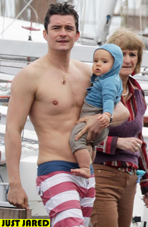 Sem camisa, Orlando Bloom passeia com o filho