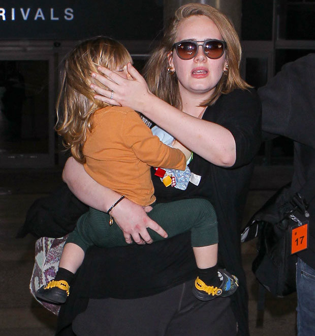 Adele esconde rosto do filho ao ser clicada em aeroporto